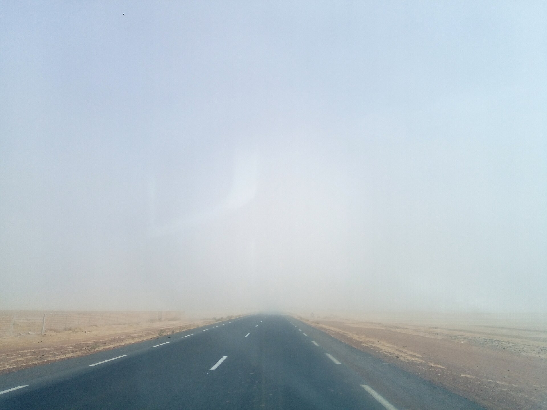 Sandstorm blåser över en asfaltsväg och gör sikten sämre.