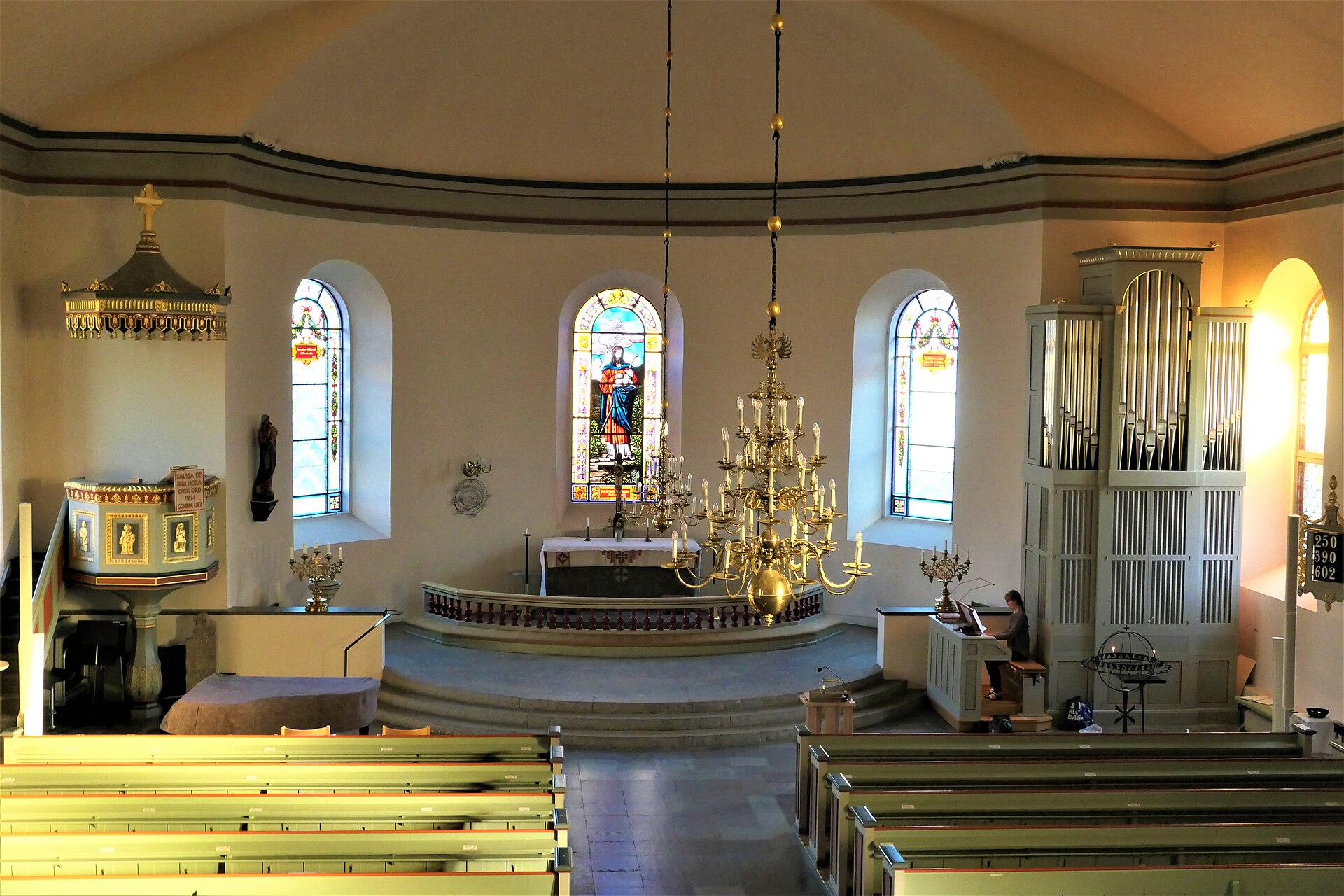 Interiör från Hjo kyrka med kyrkbänkar, altare och ljus.